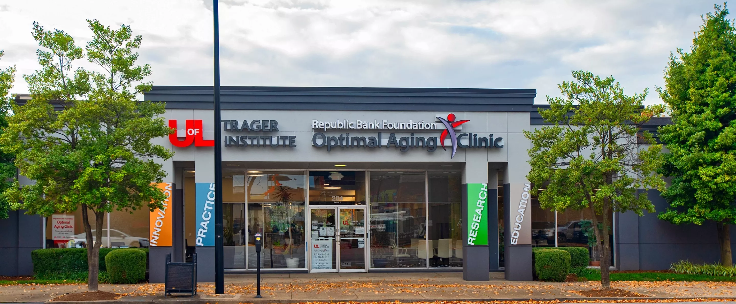 The street entrance of the Trager Institute with trees flanking both sides of the glass doorway and sign.