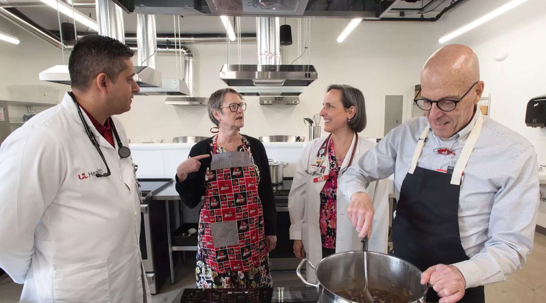 Four people standing the Trager Institute Culinary Medicine Kitchen before stove, chatting and cooking