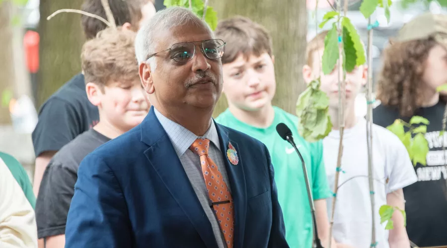 Man speaking at a podium with children and trees in background.