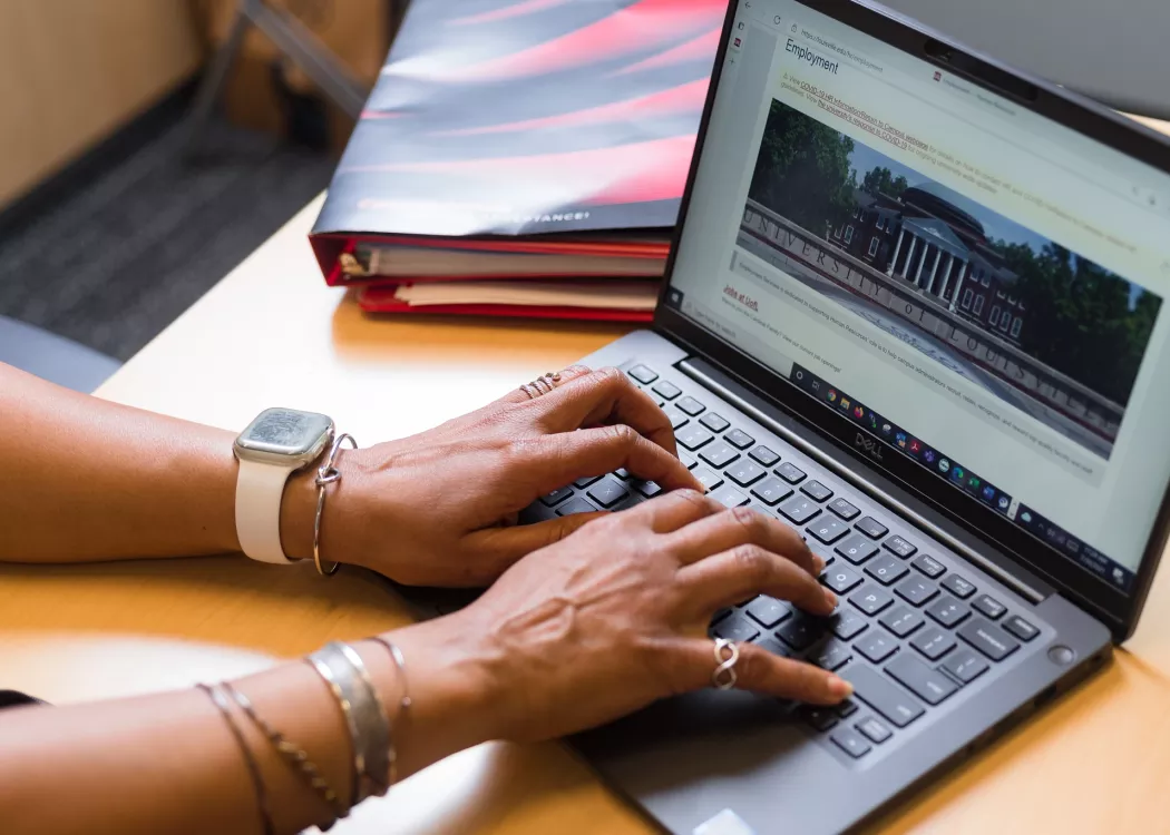 Employee typing on laptop in a UofL office