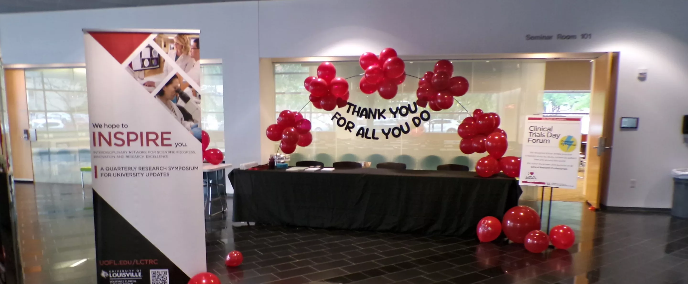 A hallway setup with a banner, red balloons, and signs for a clinical trials forum.