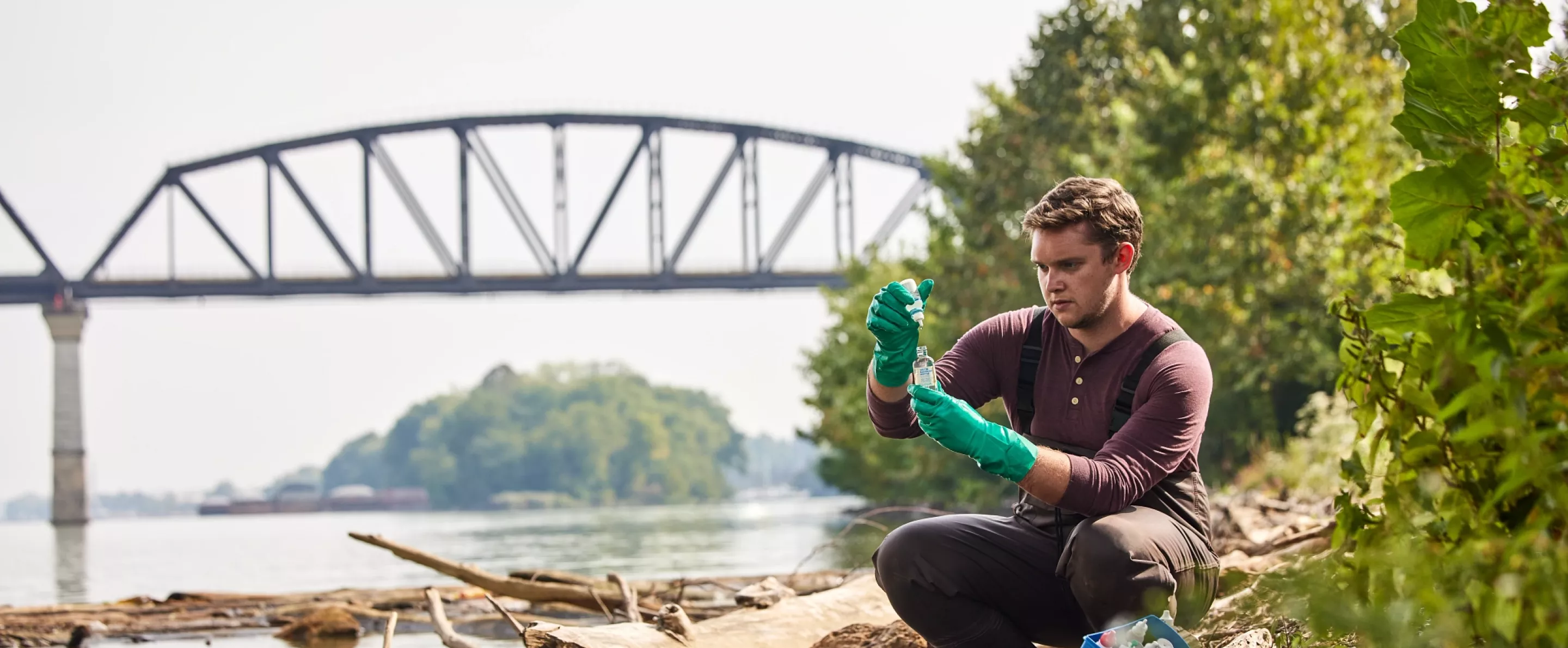 Sam Kessler is testing the water at the Ohio river as he sits close to the edge of the river to retrieve and test the sample.