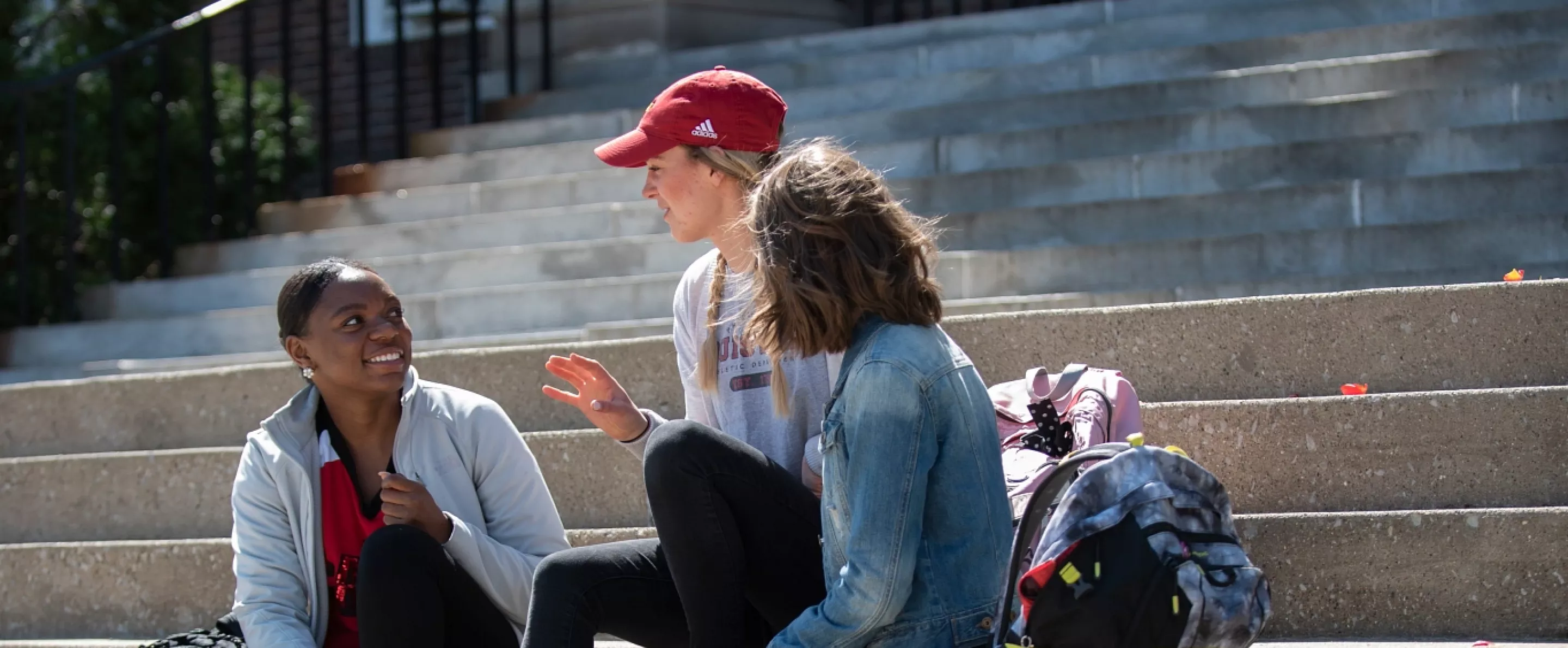 Three girls sit on steps outside and socialize