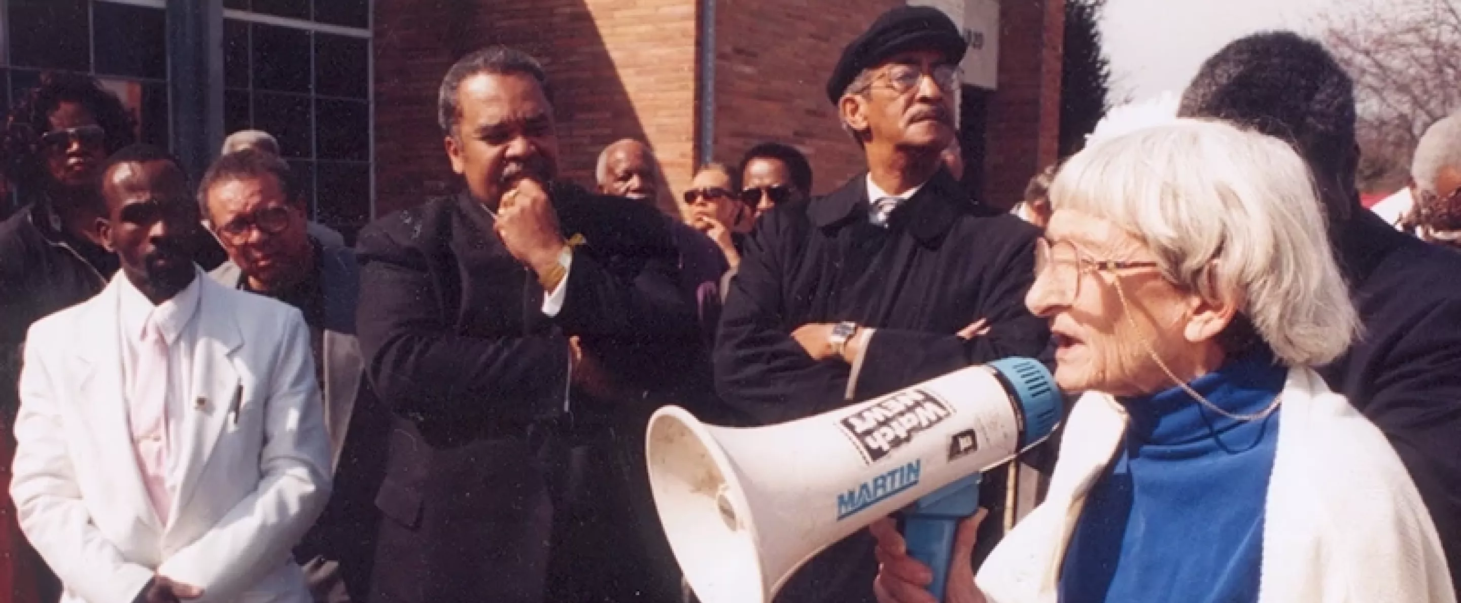 Anne Braden stands in an organized crowd with a megaphone