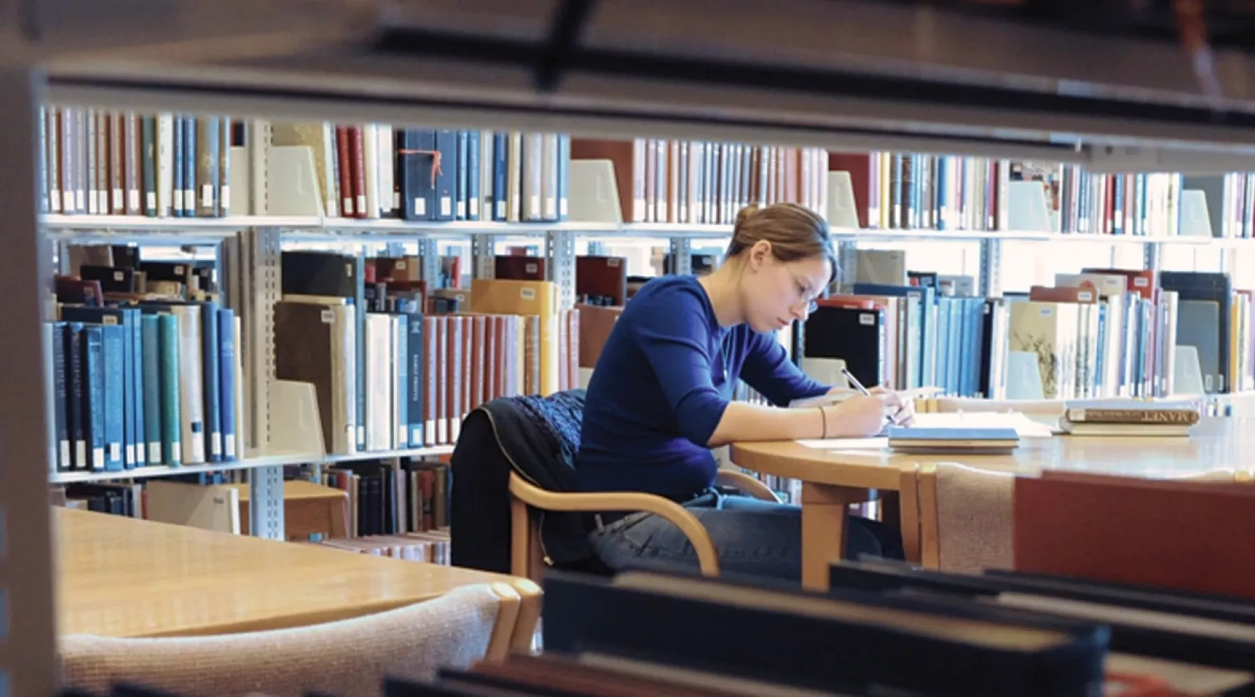 Student sitting at a table and reading in a library.