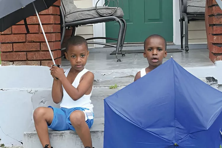 Two young children sit on a stoop holding umbrellas