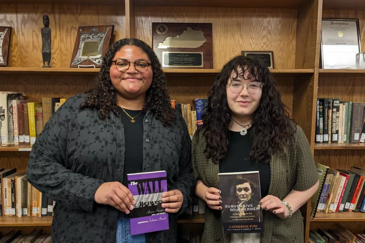 Two students posing with books for their research in the library