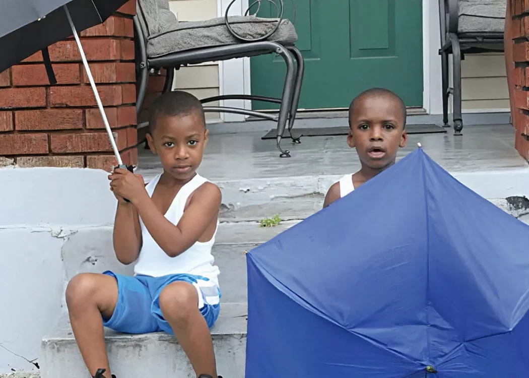 Two young children sit on a stoop holding umbrellas