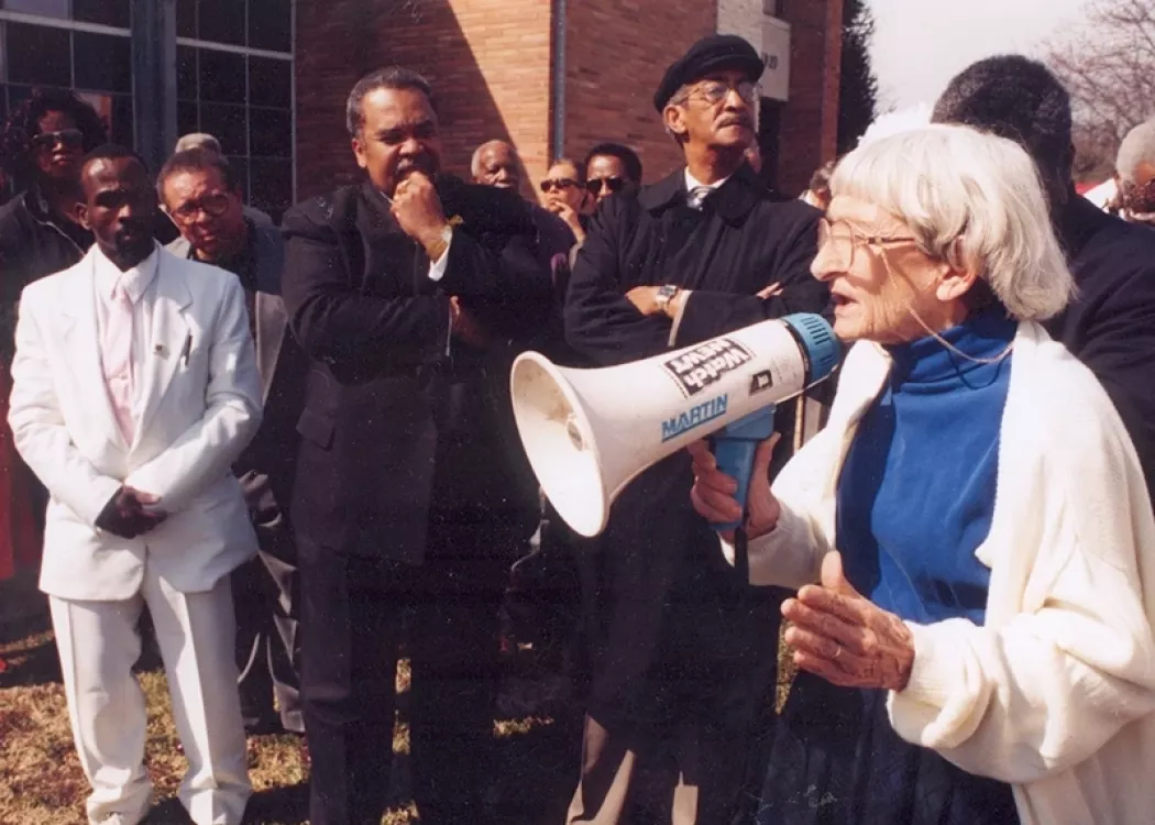 Anne Braden stands in an organized crowd with a megaphone