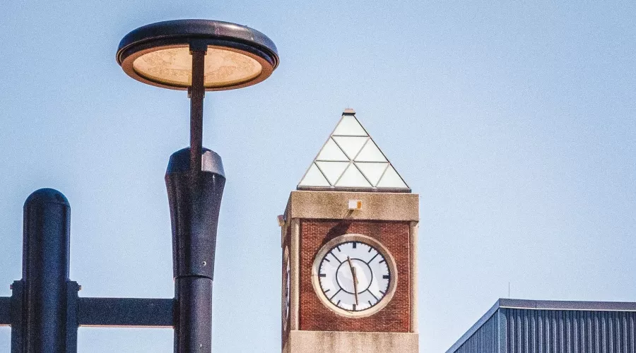 UofL clocktower and corner of the student activities center pictured in the background of a UofL lamppost banner reading "Here & Beyond".