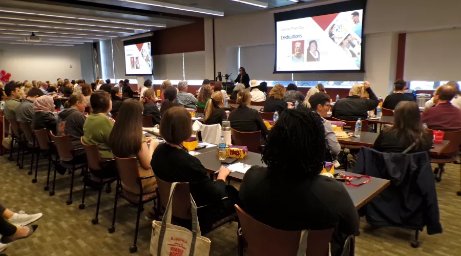 Reseach conference room filled with attendees watching a presentation titled "Clinical Trials Day."