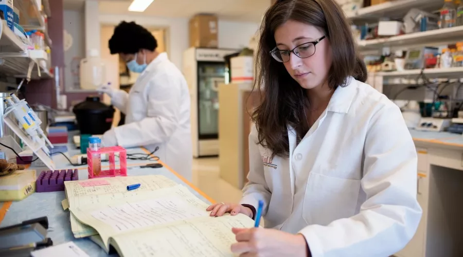 Woman writing in a lab setting.
