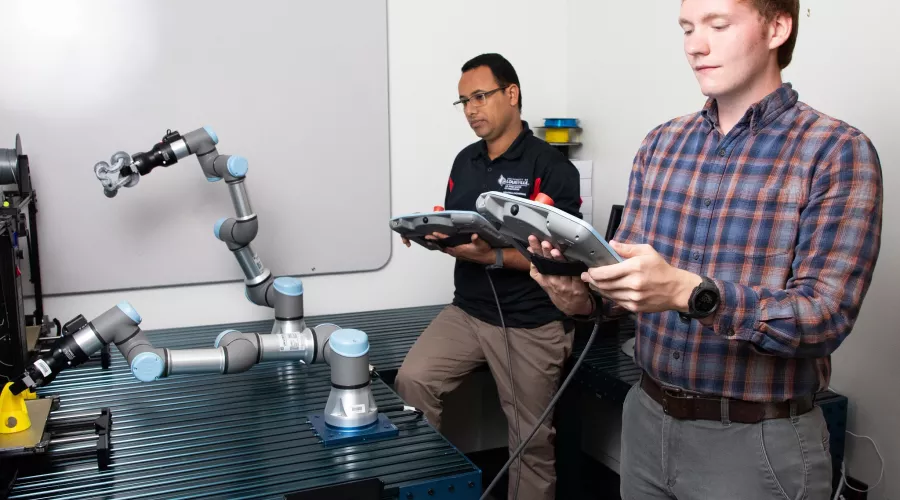 Two researchers in a lab controlling a robotic arm