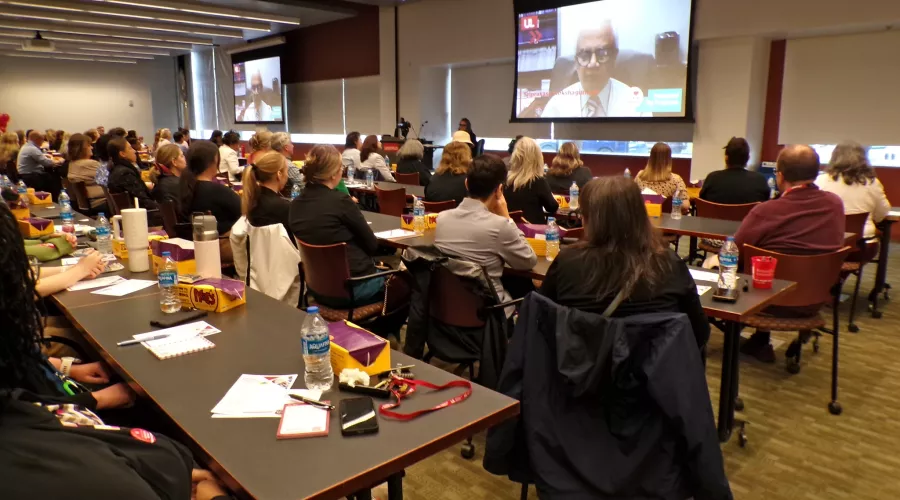 A conference room with attendees watching a video presentation on a large screen.