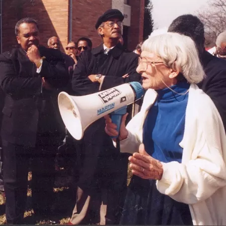 Anne Braden stands in an organized crowd with a megaphone